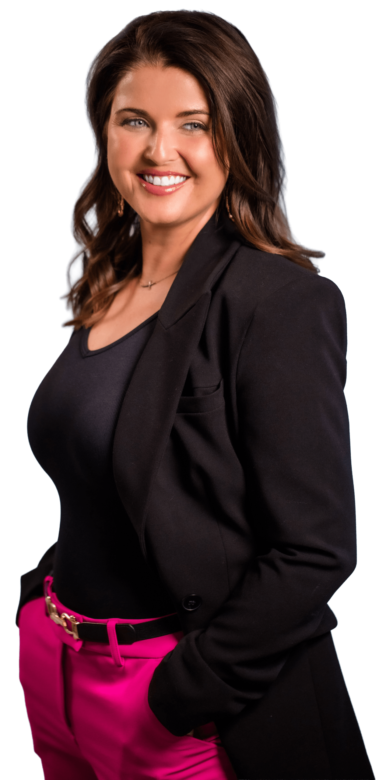 Confident professional woman smiling, wearing a black blazer and pink pants, posing with hands in pockets against a neutral background.
